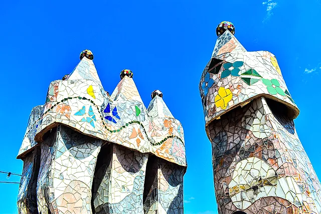 Two of the mosaic-covered chimneys on the roof terrace of Casa Batlló against a deep blue sky