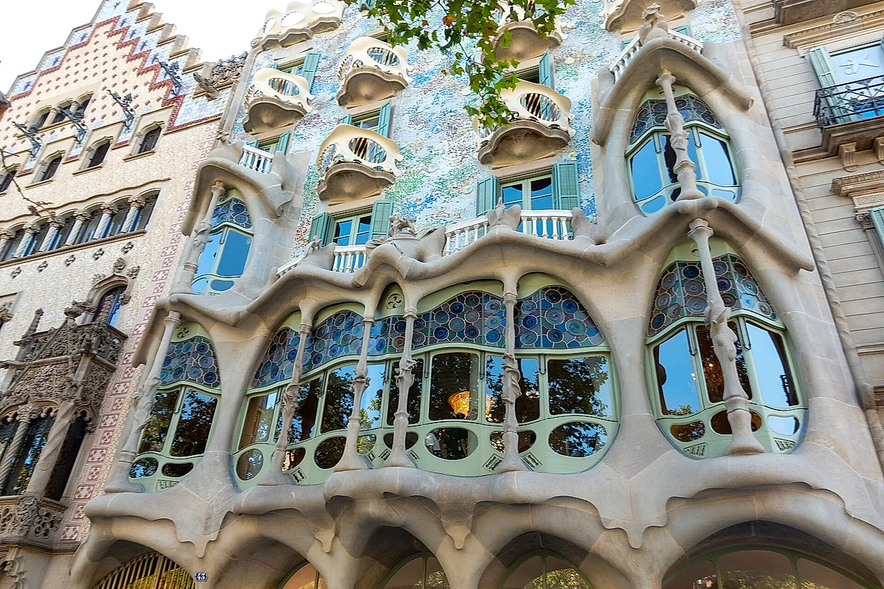 The main facade of Casa Batlló on Passeig de Gràcia in daylight, with its wavy stone balconies, blue-green mosaic wall and tiled roof