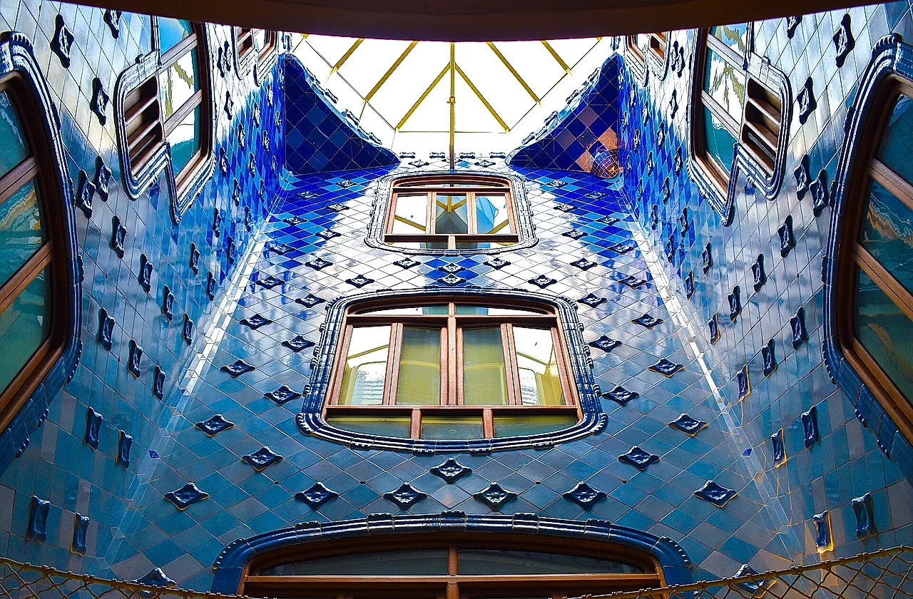 The central light well of Casa Batlló, its walls covered in tiles that shade from deep blue at the top to paler blue below, with the skylight above