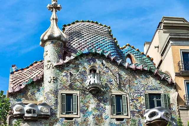 The roofline of Casa Batlló seen from the street: the tiled dragon's back, the tower with its cross and the mosaic wall below